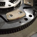 Mechanic inspecting a worn clutch assembly beside a car in an auto repair shop