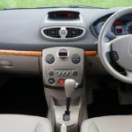 Mechanic checking a sedan's gear selector beside the driver door in natural light.